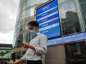 Pessoas passam em frente a tela mostrando cotações de ações na fachada do prédio da bolsa de Hong Kong