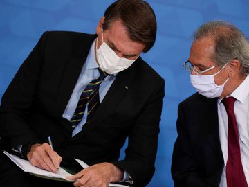 O presidente Jair Bolsonaro conversa com o ministro da Economia, Paulo Guedes, durante cerimônia de anúncio de medidas da Caixa Econômica em apoio a hospitais filantrópicos, em Brasília, 25 de março d