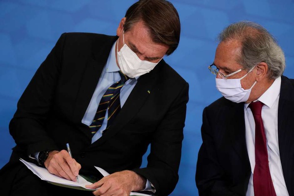 O presidente Jair Bolsonaro conversa com o ministro da Economia, Paulo Guedes, durante cerimônia de anúncio de medidas da Caixa Econômica em apoio a hospitais filantrópicos, em Brasília, 25 de março d